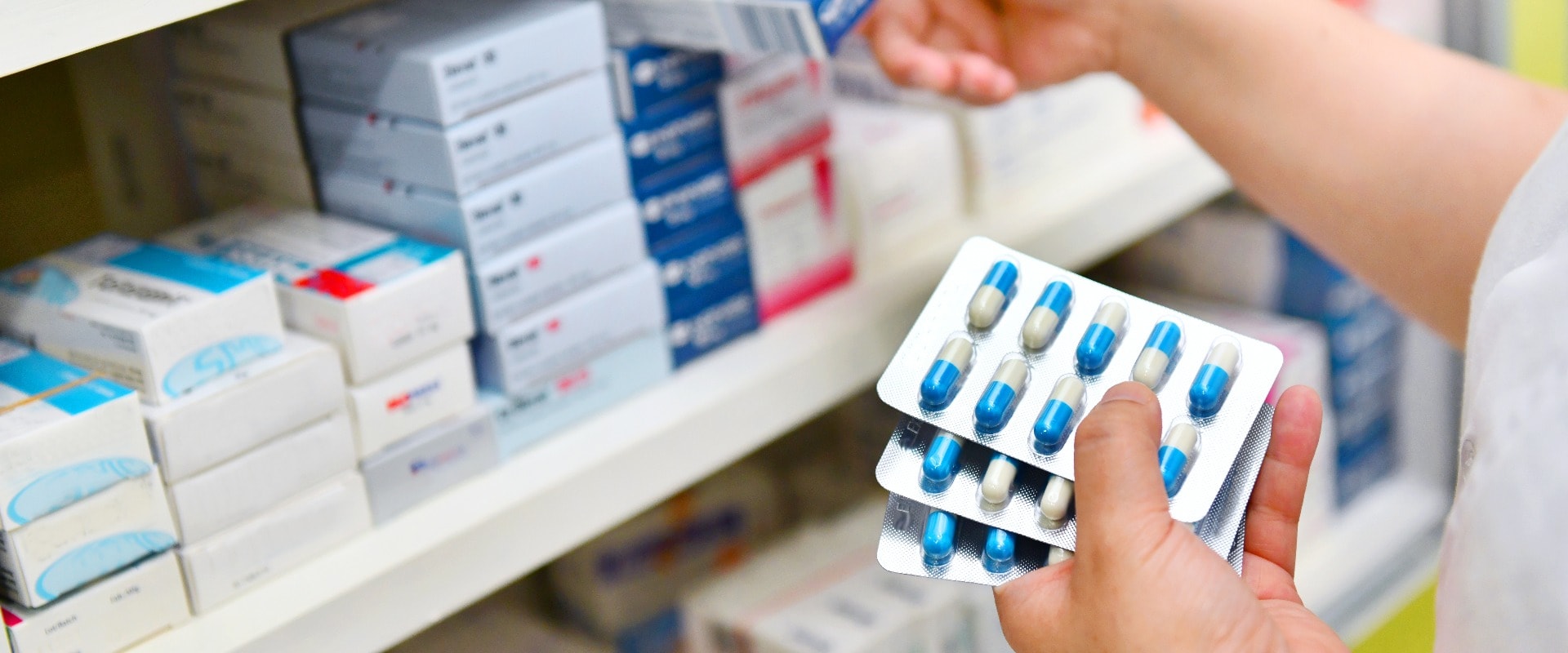 Pharmacist holding medicine box and capsule pack in pharmacy drugstore.