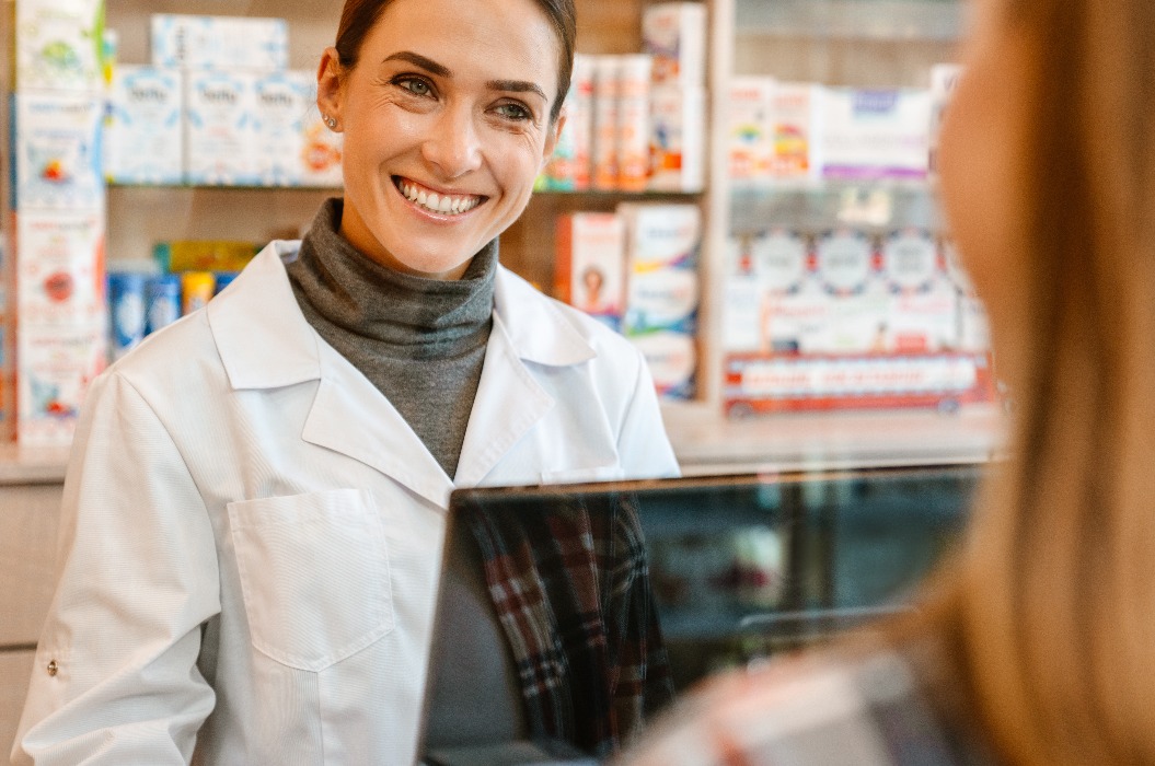 Eine Apothekerin im weißen Laborkittel, die in einer Apotheke mit einer Kundin spricht.